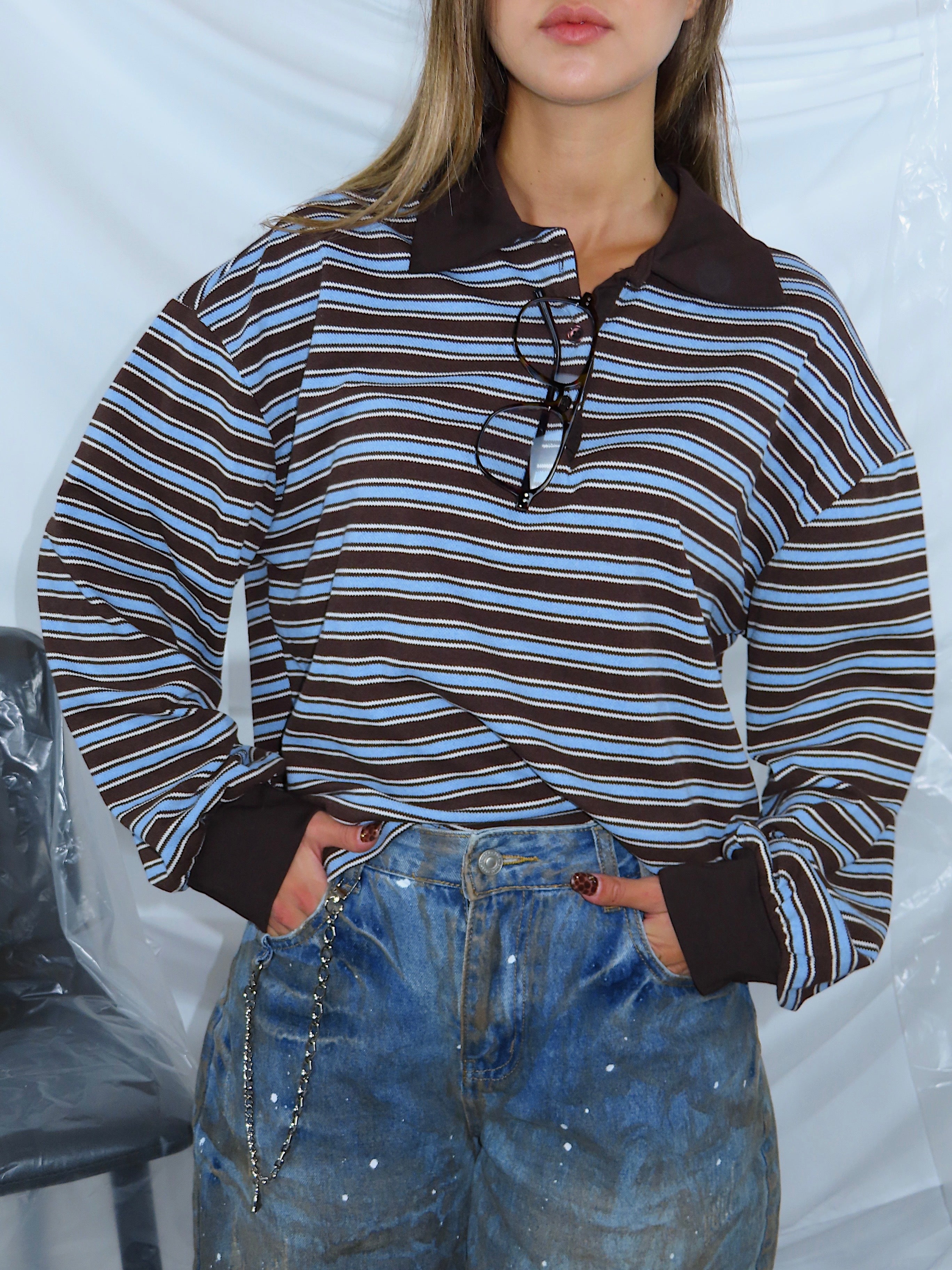 Primo piano frontale di polo a righe celeste e marrone indossata da modella, colletto a polo e bottoni.
