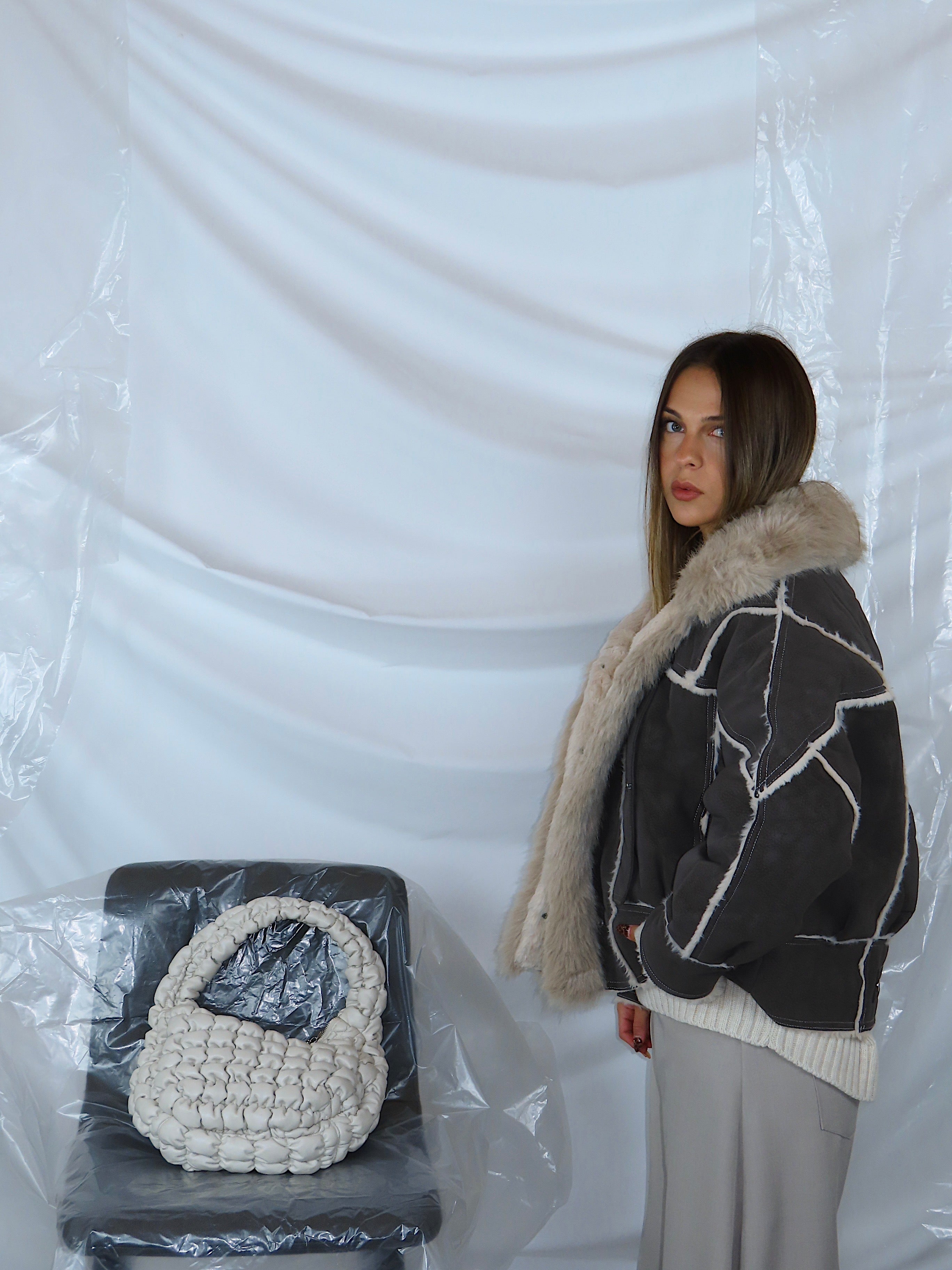 Zoom laterale su giacca aviatore grigia scura a mezzo busto, evidenziando colletto imbottito, tessuto martellato e finiture.