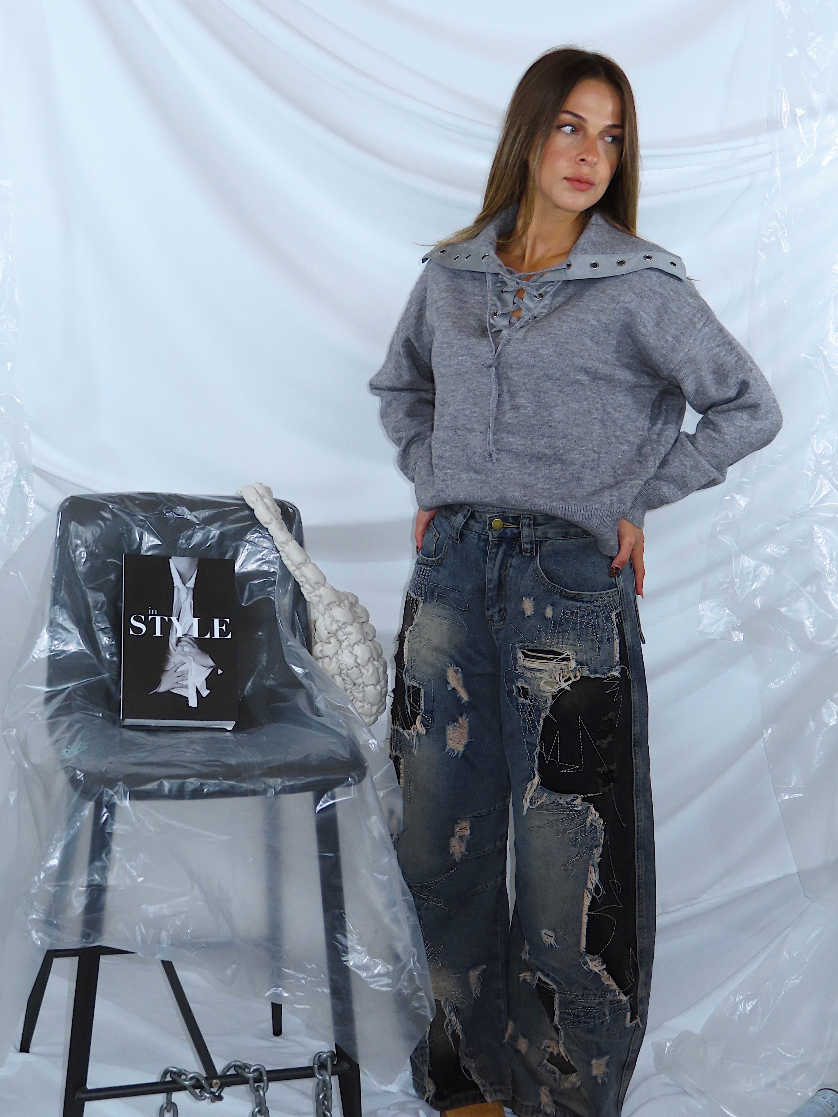 Outfit da donna con maglione grigio e jeans in denim, indossato da modella in piedi, vista tre quarti.