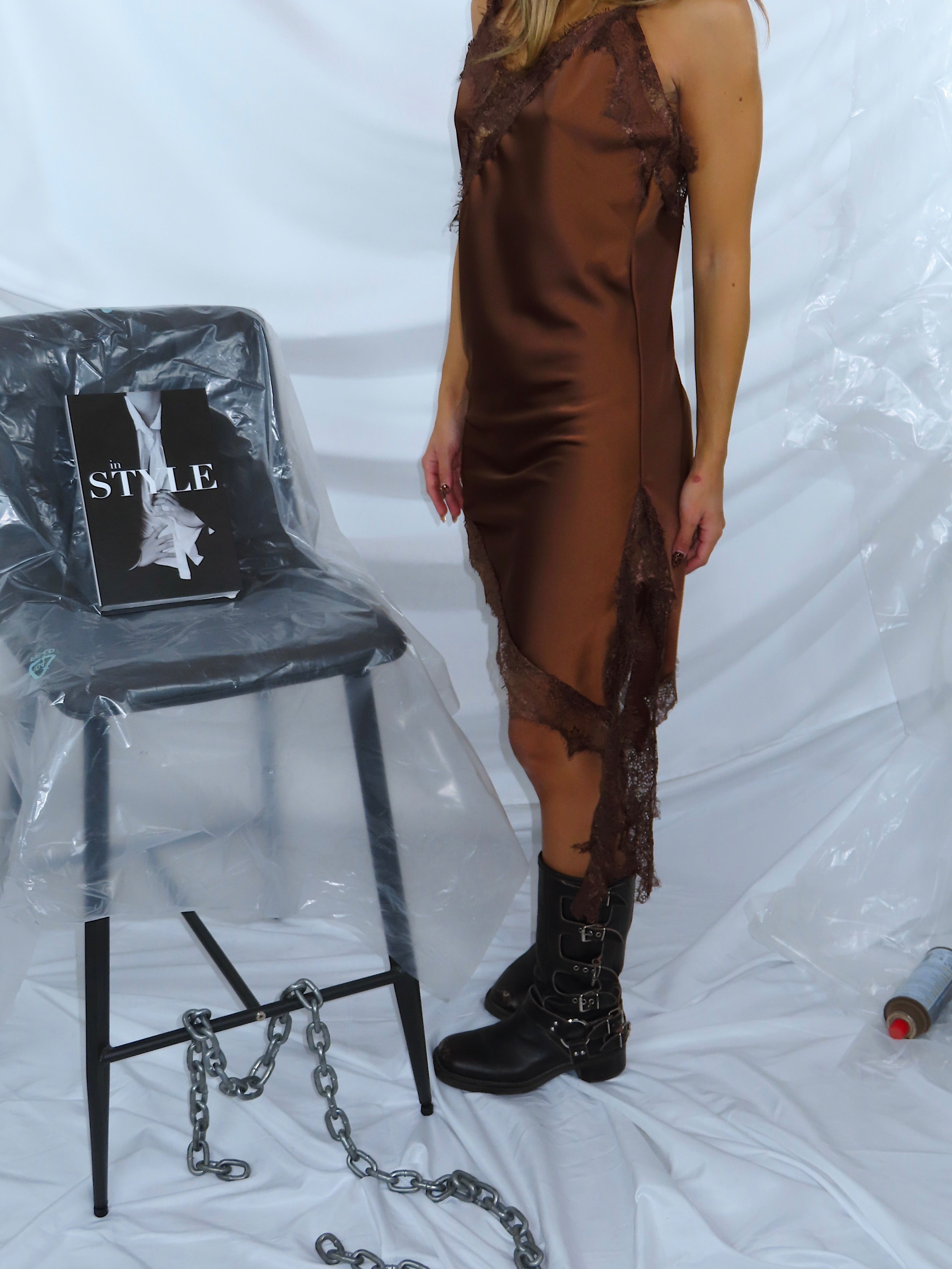 Primo piano dei motivi in pizzo su abito asimmetrico in raso marrone, evidenziando il design.