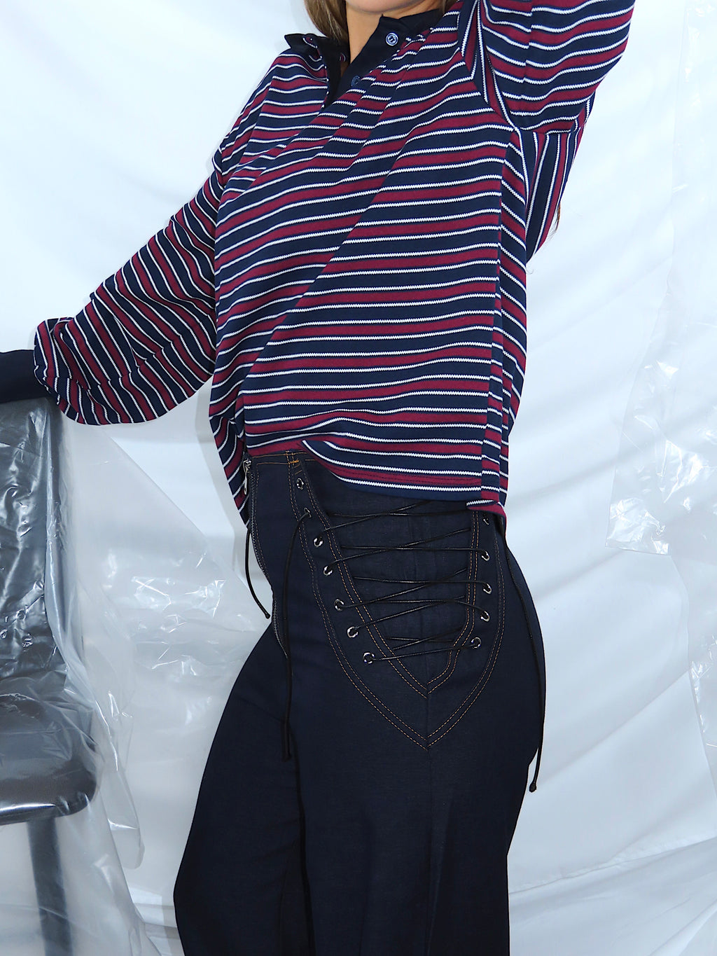 Dettaglio laterale di pantaloni in denim con lacci decorativi sui lati, tessuto robusto e cuciture visibili.