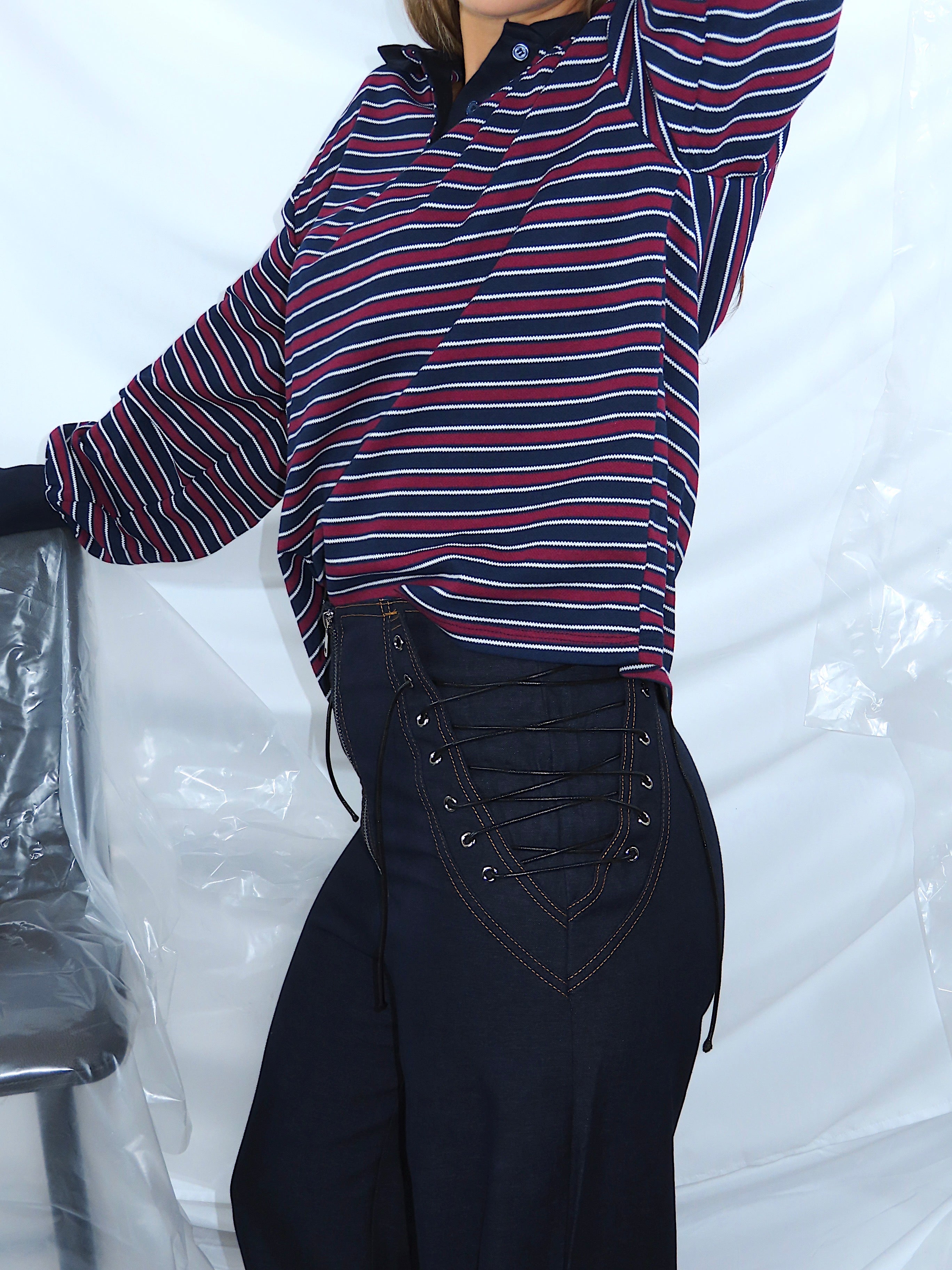 Dettaglio laterale di pantaloni in denim con lacci decorativi sui lati, tessuto robusto e cuciture visibili.