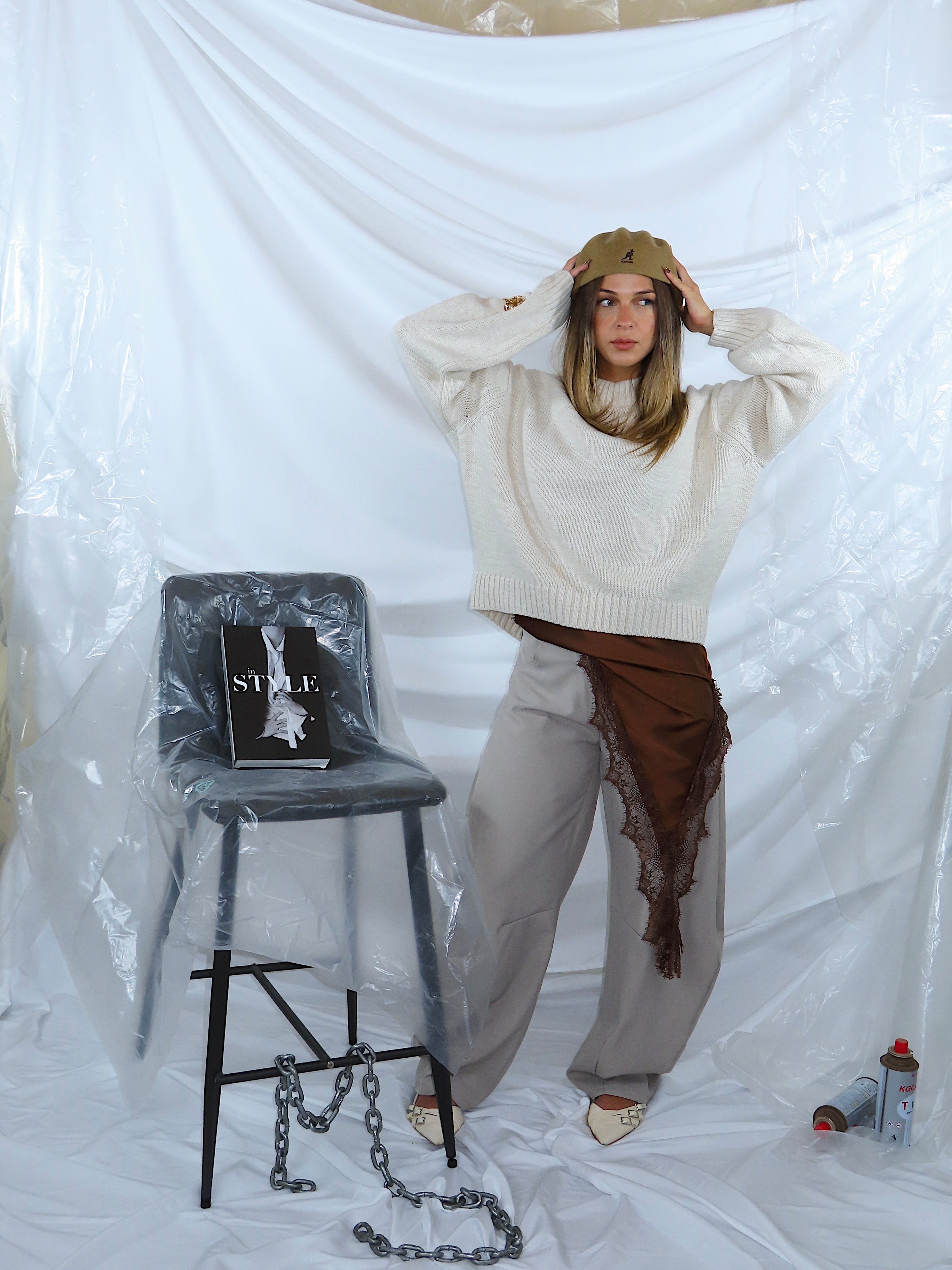 Look da donna con maglione color panna, pantaloni grigi e abito marrone, inquadratura frontale.